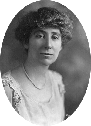 Photo of Jeannette Rankin wearing a scoop neck dress with pearls. Her dark hair is cut at the top of ear level.
