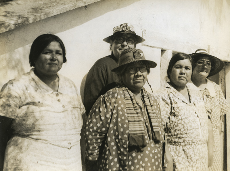 5 Native American women pose before a white wall.