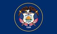 Utah flag has the state seal on a blue background. A bald eagle perches atop a shield and clutching arrows. A beehive with lilies on right and left is in the center above the year 1847 and 1896.