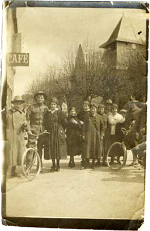 American soldiers pose with ladies and bicycles on a street in front of a cafe in France.