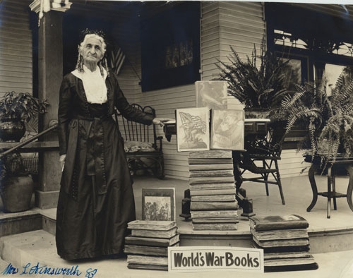 83 year old woman standing on the steps of a porch next to a stack of books. 
