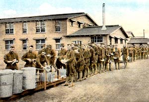 Soldiers wash dishes in a long line around barrels outside.