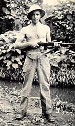 Shirtless man in pith helment holding gun.