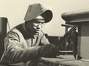 Black worker welding something while wearing safety gear such as a helmet and goggles.