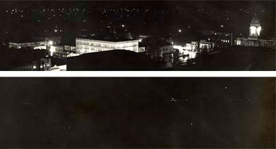 In top image many lights can be seen illuminating clearly buildings. In bottom image only a few pin points of light show.