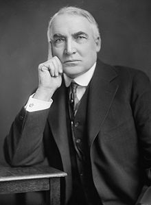 Warren G. Harding in a suit and tie leaning on a table with one elbow.