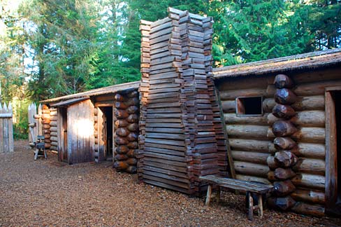 Long log cabin with multiple doors in wooded setting.