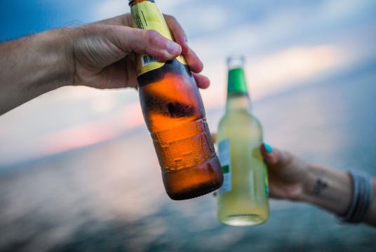 Two hands hold up glass bottles with the ocean in the background.