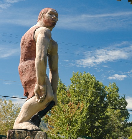 Fiberglass caveman statue with green trees in background and blue sky.