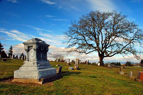 Stone grave marker on left with oak tree in background on right. Smaller stone caps marking graves surrounding.