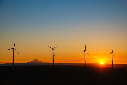 Four wind turbines shown with a colorful sunset in the background.