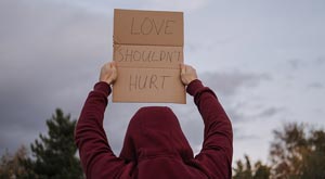 Person from behind wearing maroon hoodie holding a sign that says Love Shouldn't Hurt.