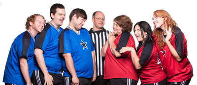 ComedySportz Players dressed as opposing sports teams with a referee between them.