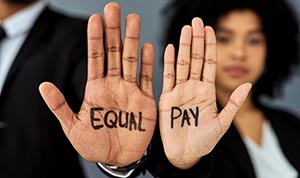 Two hands held with palms facing the viewer that have Equal Pay written on them