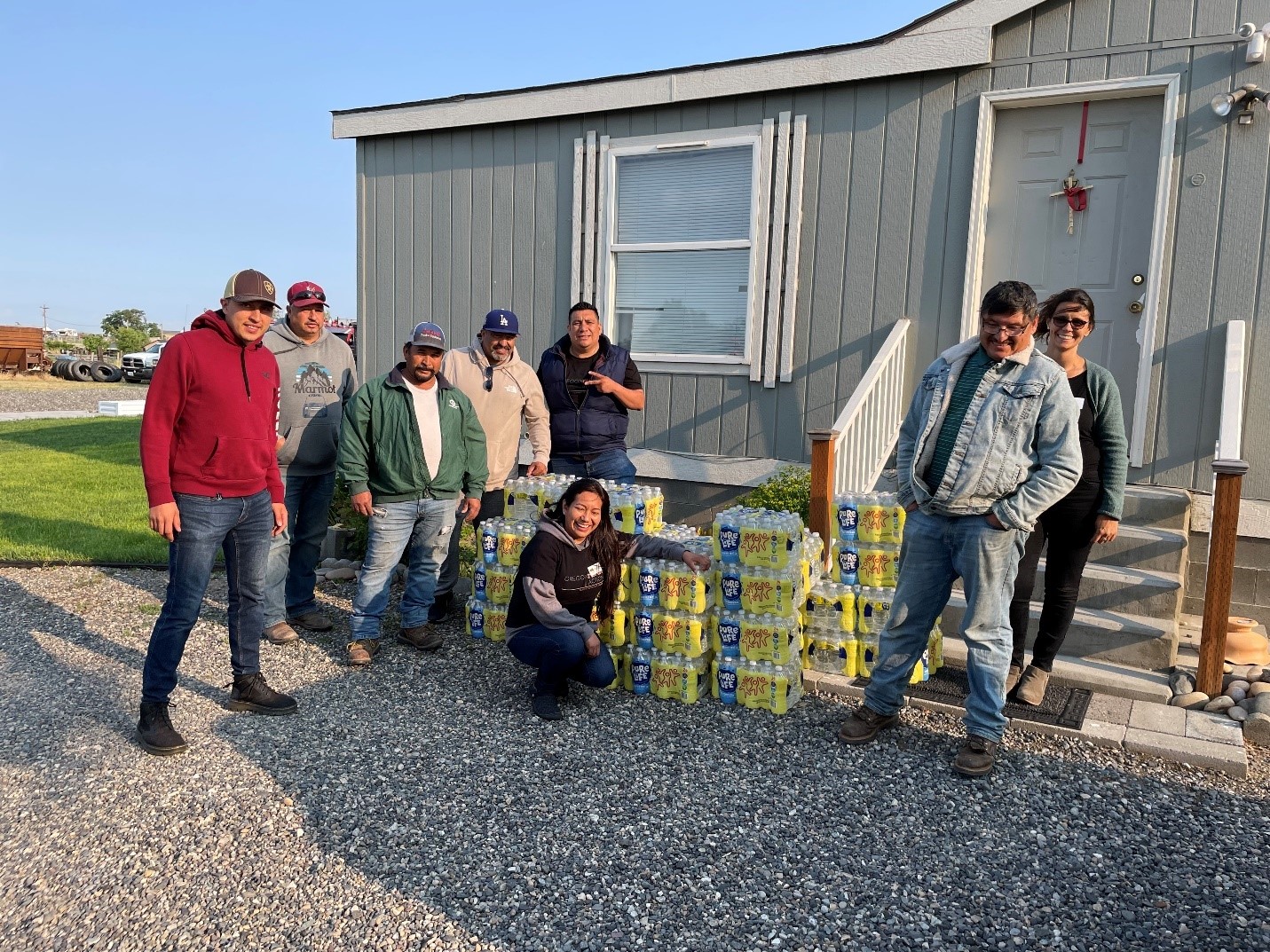 8 people stand in front of a building with packages of bottled water.
