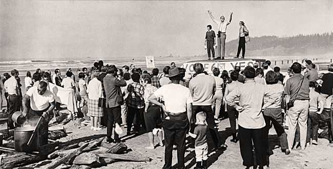 Photo of 3 people standing atop a van speaking to a crowd of people at the beach. Sign on van says: "Vote 6 Yes"