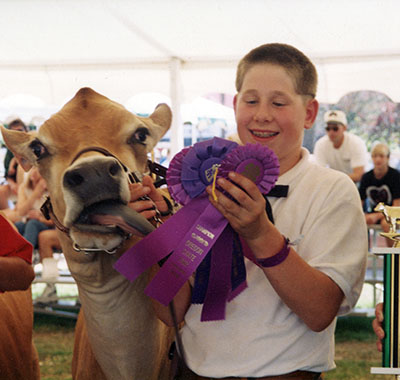 A boy stands with his cow and ribbons