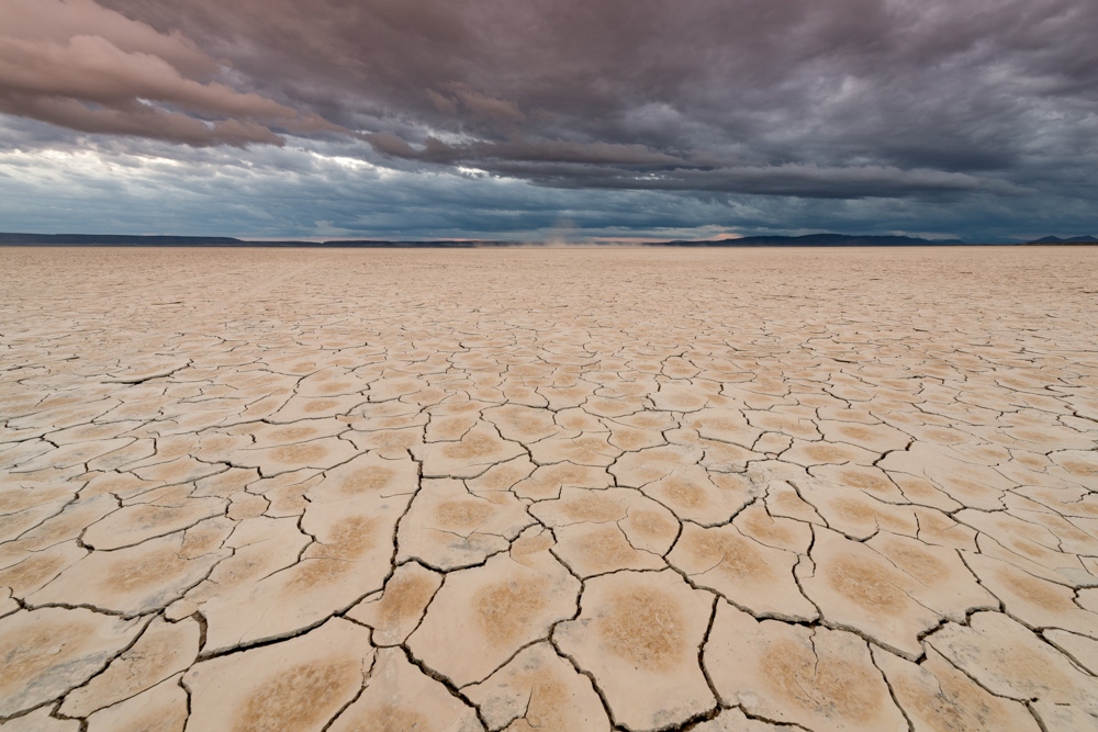 Dry lake bed showing cracks in the earth. A sky filled with dark clouds above.