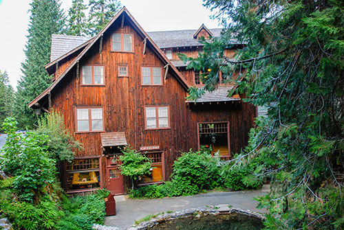 Rustic lodge covered with bark from cedar trees. Shed and dormer style roofs mimic the surrounding mountains.