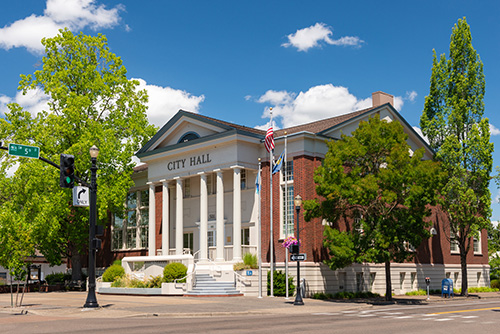 3 story historic City Hall building in colonial style with 6 pillars holding up the overhang above front door. Brick walls.