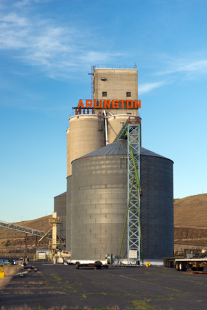 Grain elevator with 'Arlington' sign in big letters on top. Set in a high desert landscape with yellow grass surrounding.