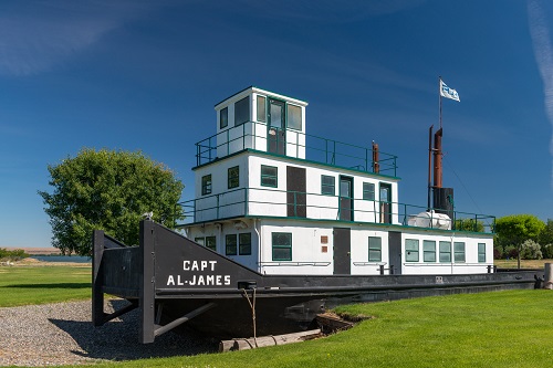 A tug boat with 3 levels of deck and "Capt. Al. James" printed on the side rests in a grassy area of a park.