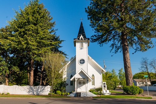 White-frame building with bell steeple in classic Gothic Revival Style.