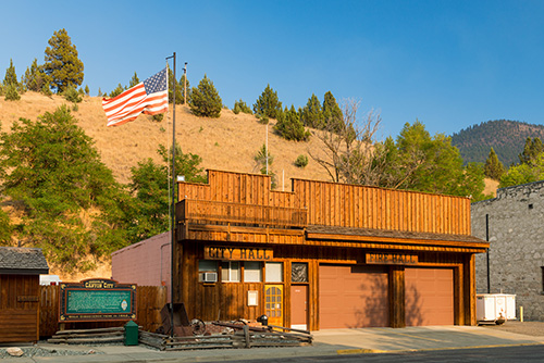 A one story building with old west style false front wood architecture. One side labeled City hall the other Fire Hall.