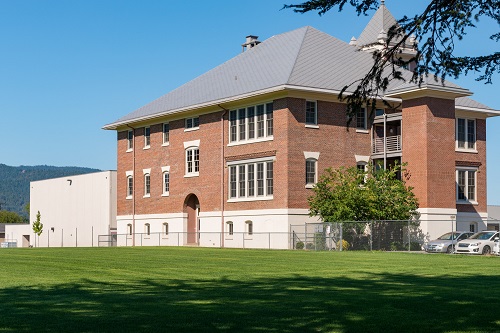Three-story brick building with a grassy lawn in front.
