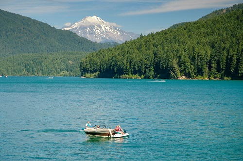 A few people on a personal boat on a lake with Mt. Jefferson seen in the distance. The mountain is snow capped.