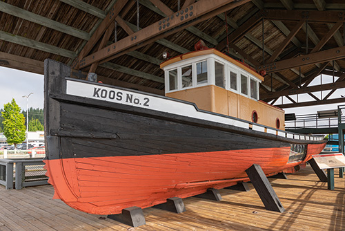 A retired tug boat on display under a wooden roof.