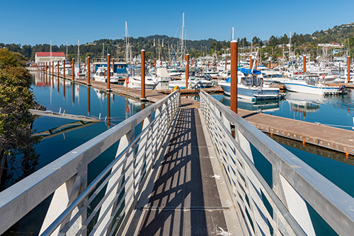 View from the top of a walkway leading to a harbor with boats.