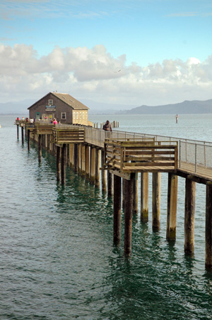 A wooden pier reaching out into a bay with a building at the end that served as a boathouse from 1934-1960s.