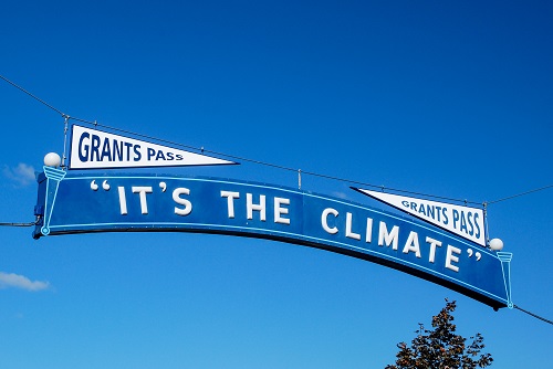 A sign reads Grants Pass It's the Climate. Blue Sky behind.