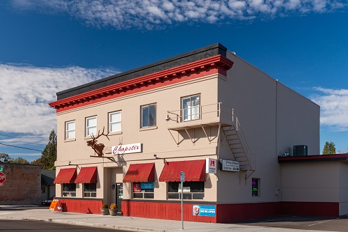 A two-story building with a sign on the front reading Chopstix. Red awnings over the 4 windows in front.
