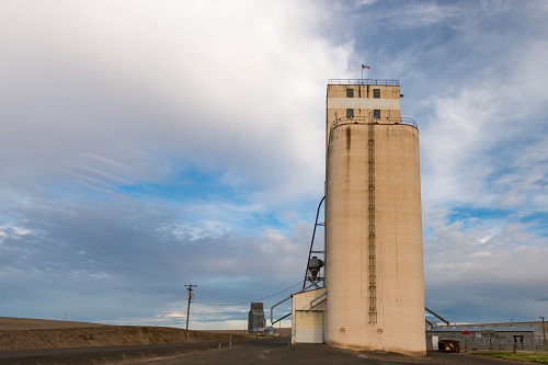 Grain elevator next to a road on a flat and desolate landscape.