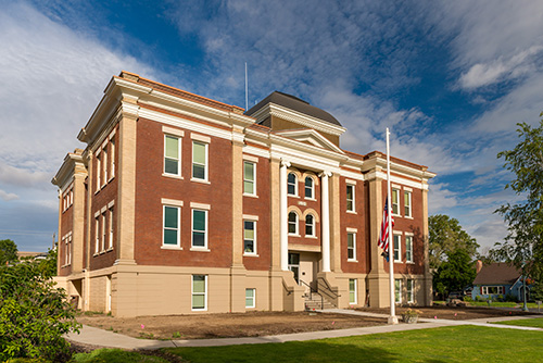 A classic red brick building with white trim and a central pediment featuring a cupola on top. The building has two visible floors with symmetrically placed windows and a set of stairs leading to the main entrance.