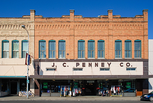 Two-story brick building with J.C. Penny Co. written across. Racks of clothing on the sidewalk.