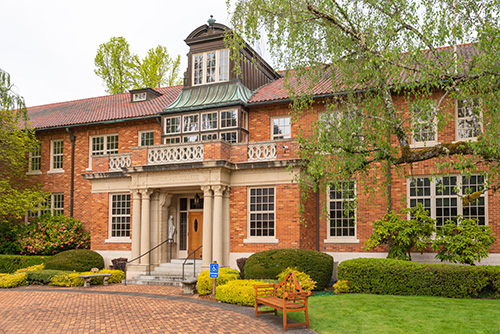 A two-story brick building with a central entrance flanked by white columns and topped with a decorative cupola.