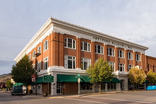 Three-story brick, early commercial style building. Building takes up city block. Front door at an angle to corner of sidewalk. 