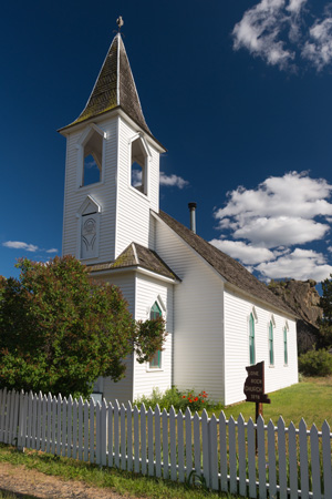 A 1 room church with steppled bell tower stands in front of the large rock for which Lonerock is named.