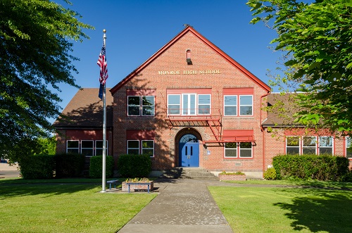 Two-story brick school building. Arched front opening with double doors. Grassy lawn and walkway lead up to school. 