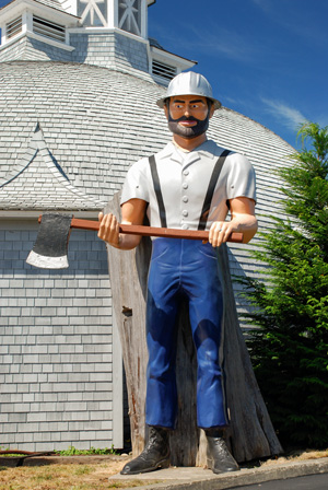 A logger statue of fiberglass as tall as a 1-story building stands outside the Logging Museum. The museum dome-shaped.