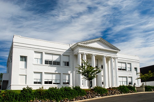 Building resembling a Greek Temple at the top of a hill. Pure white, the buillding is solid and square with fluted Ionic columns across the front that support a classical peiment. 