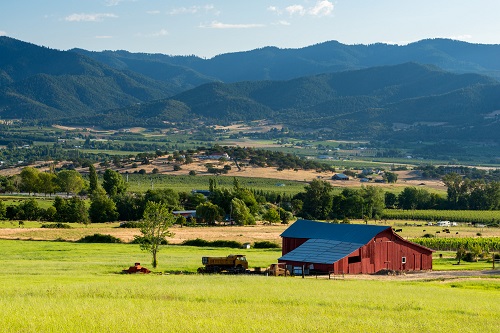 A farm house in a field with gently rolling mountains in the distance. The mountains are covered in evergreen trees.