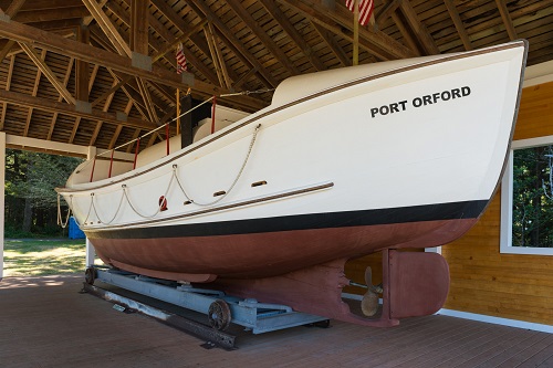 Coast Guard lifeboat on a platform with wheels inside a wood building built to house the boat. "Port Orford" is printed on side.