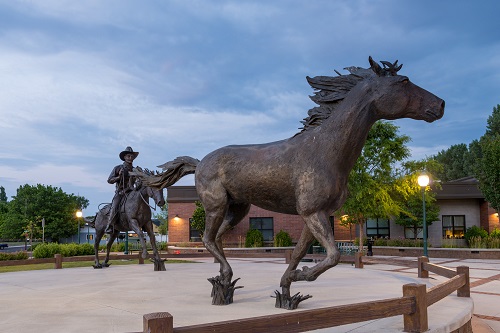 A sculpture of a cowboy on a horse chases after a wild mustang.