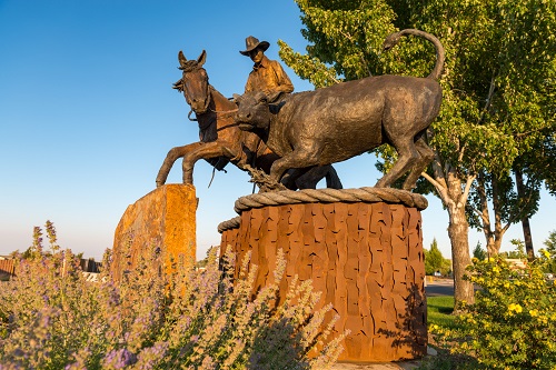 Bronze sculpture of cowboy on horse herding a calf.