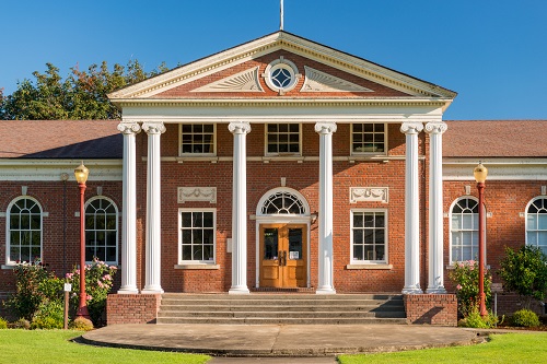 Horizontally-oriented brick building has a central, projecting full, 2-story portico with gable roof, supported by 6 columns. 