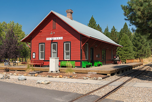 Single-story building with wood walking platform reaching to edge of train tracks.